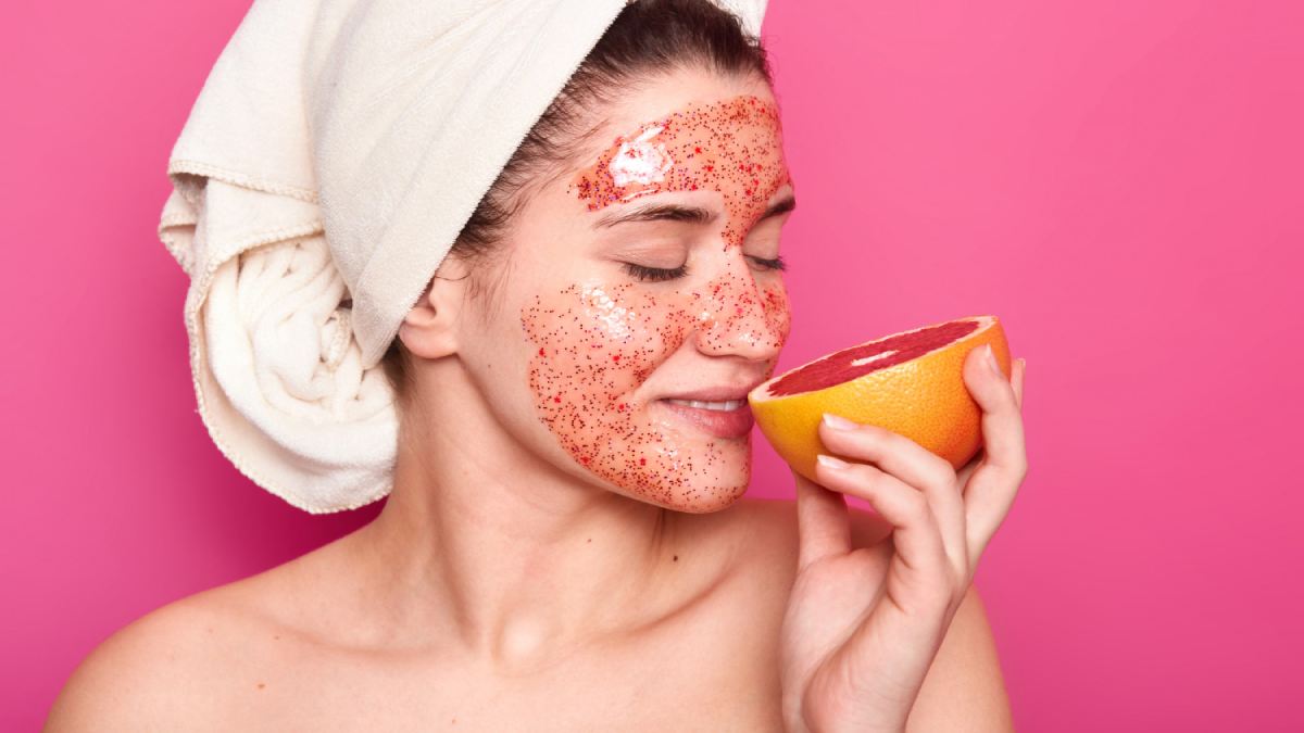 Beautiful woman using face scrubs on her skin while keeping an apple in hand
